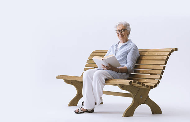 istock An elderly smiling and happy woman sitting on a bench is reading a book. 2232468794