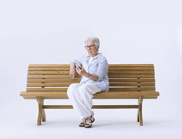 istock An elderly woman looks at her phone while sitting on a bench. 2232469067
