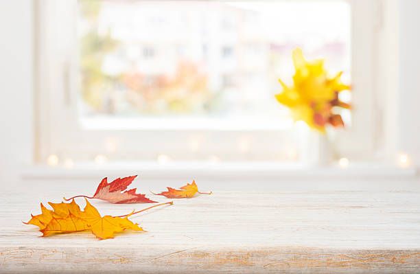 Autumn leaves on wooden table with copy space over blurred window sill background