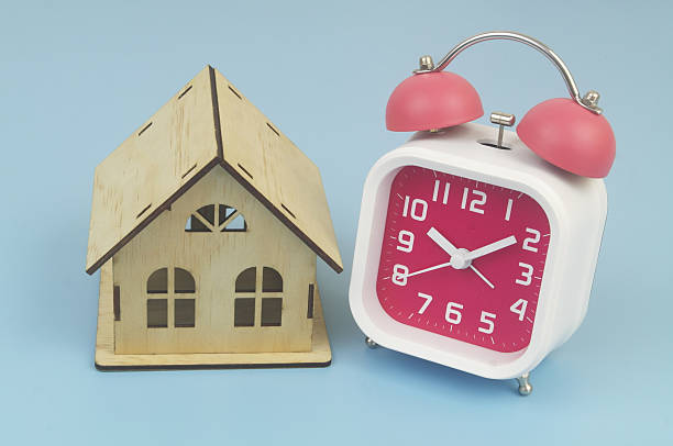 istock Alarm clock and wooden house model on blue 2232469353