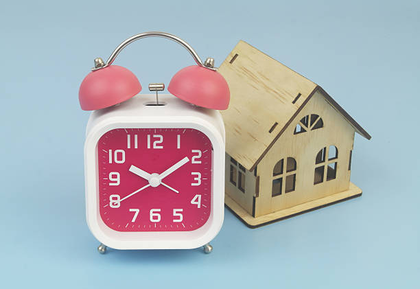 Alarm clock and wooden house model on blue background.