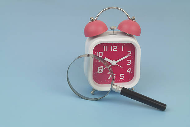 istock Alarm clock under magnifying glass on blue 2232469490