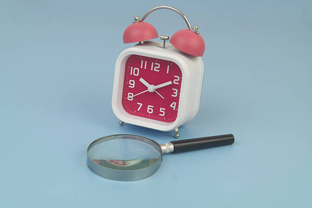 istock Alarm clock and magnifying glass on blue 2232469509