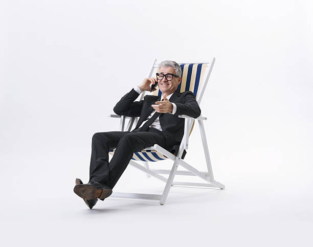 Manager in a black suit talking on the phone while sitting on a beach chair, isolated on a neutral background