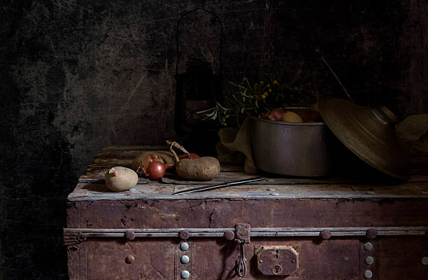 Still life. Potatoes, knife, pan and onions lie on a vintage box close-up on a dark background