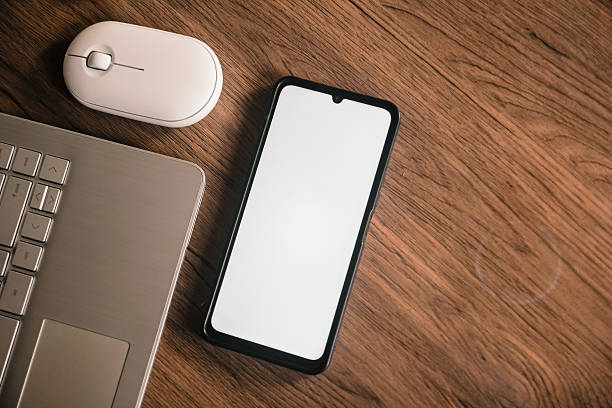 istock Smartphone with blank screen next to a laptop and mouse. 2232475702