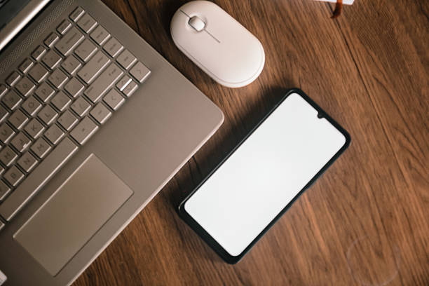 istock Smartphone with blank screen next to a laptop and mouse. 2232475705
