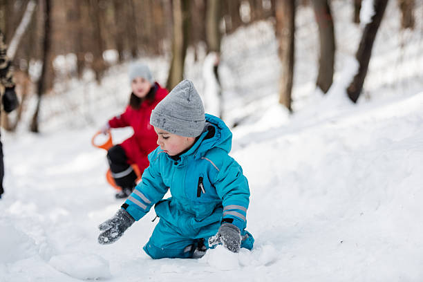 istock Child playing with snow in winter forest while sister is sledding 2232477578