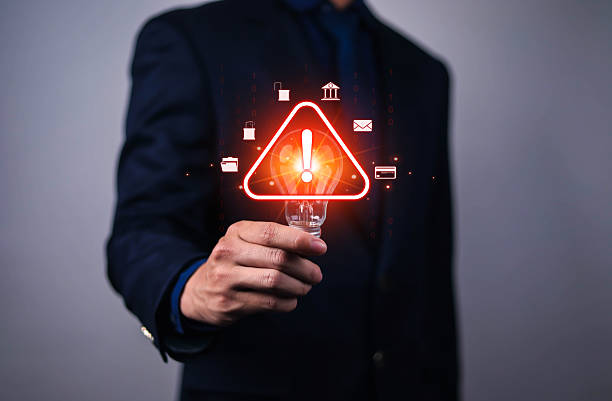 Businessman holding red warning alert icon with cybersecurity symbols, representing digital risk, data protection, hacking threats, online fraud, and information security awareness in modern business.