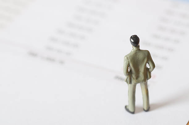 istock Corporate Decision-Making Visual: Miniature Businessman Reading Financial Summary 2232481788
