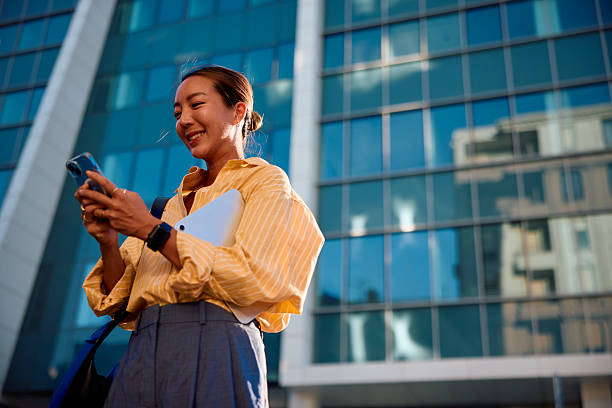 istock Smiling businesswoman using smartphone in front of modern office building 2232482015