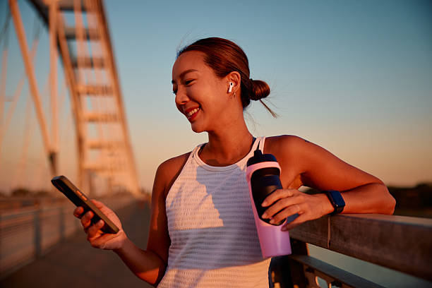 Young sportswoman using smartphone after training on bridge at sunset