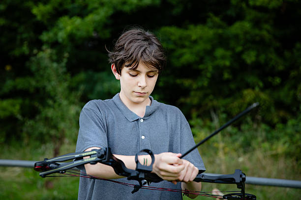 Teenage boy practicing archery with bow and arrows outdoors. Young male learning traditional sport activity, focus and concentration. Real life, real people lifestyle concept