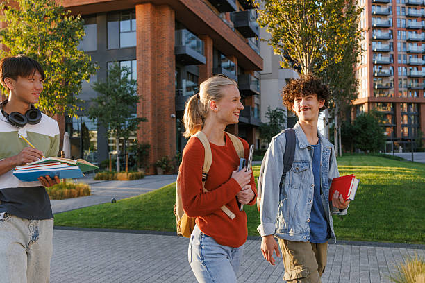 Two cheerful multi-ethnic students running in the university campus, holding books and backpacks, probably late for class, smiling and looking forward