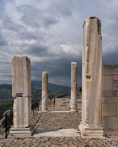 Trajaneum, Pergamon Acropolis, Turkey. Ancient Roman temple ruins under dramatic cloudy skies, overlooking a mountainous landscape