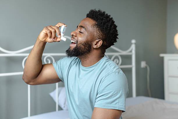 istock Man using asthma inhaler seated on a bed in a bright room 2232489061