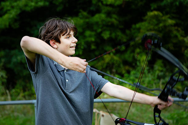 istock Teenage boy practicing archery with bow and arrows outdoors. Young male learning traditional sport activity, focus and concentration. Real life, real people lifestyle concept. 2232490245
