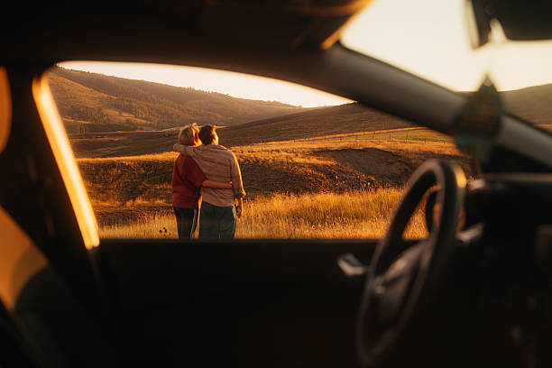Couple embracing in golden fields at sunset, framed by a car window. stock photo