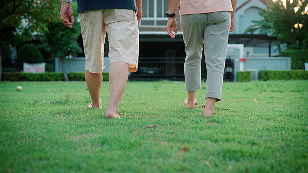 Close-up shot of an unrecognisable person's feet running along a footpath in the countryside on a frosty winter's morning. They are wearing black leggings and white sports socks with their trainers. The surrounding ground has a dusting of snow and there is another person visible in the background, out of focus.\n\nVideos similar to this scenario available.
