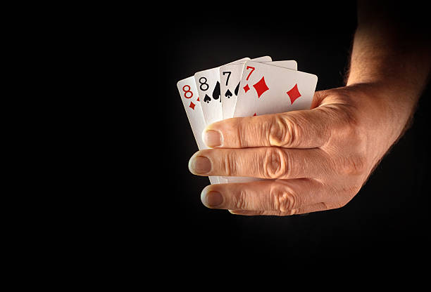 istock A hand is gripping four playing cards featuring two eights and two sevens. The setting is dimly lit, emphasizing the cards' vibrant colors and the hand's details 2232503446