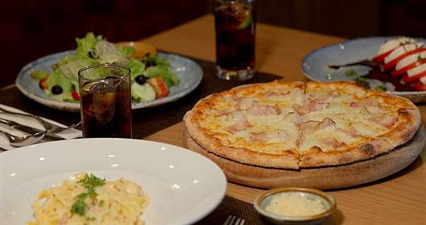 Italian cuisine spread featuring pizza, salad, pasta on wooden table.