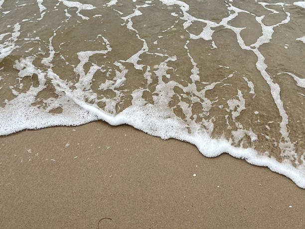 istock Close-up of white foam waves on sand background 2232516362