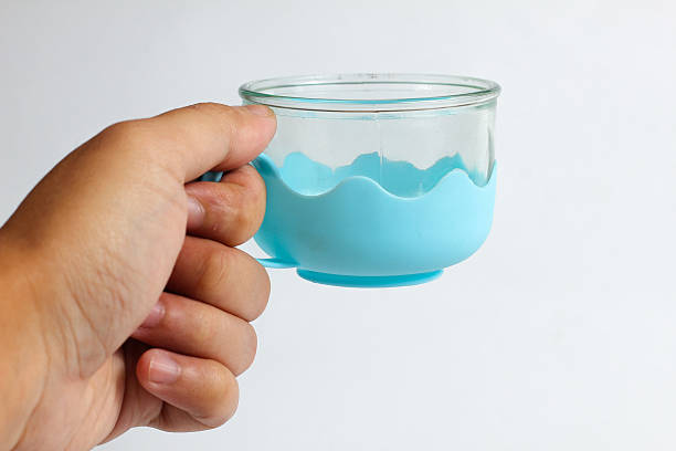 istock hand holds a clear glass baby cup fitted with a light blue silicone sleeve 2232524690