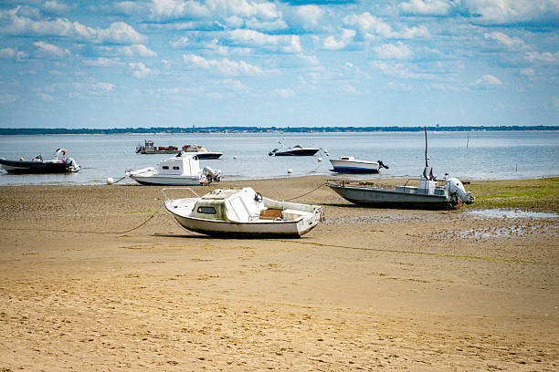 Several small boats rest on a sandy beach during low tide, surrounded by calm waters and a serene atmosphere. This picturesque seaside scene captures tranquility  on the Atlantic coast of France near Bordeaux