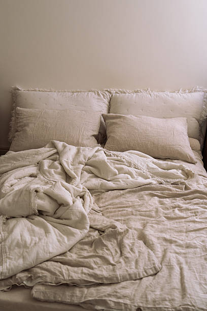 istock Double bed with crumpled oatmeal linen bedding and pillows, soft sunlight shadows creating a cozy aesthetic morning atmosphere. 2232529842