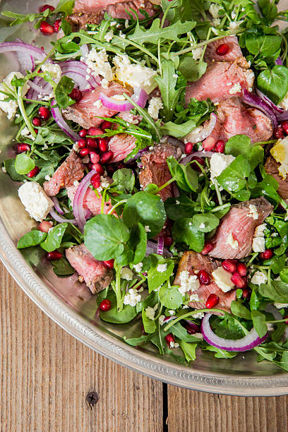 Fresh Salad with Arugula, Steak, Pomegranate, and Feta Cheese on Wooden Background
