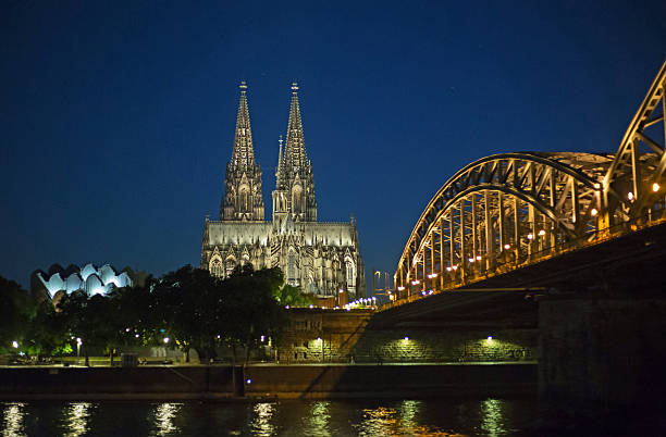 Night time view of Cologne Cathedral and bridge, illuminated with reflection in the River below