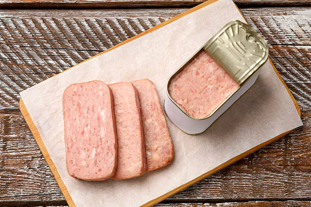 Canned meat in tin can on wooden table, top view