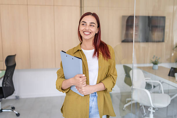 istock Young woman smiles confidently while holding a clipboard in a modern office setting 2232536930