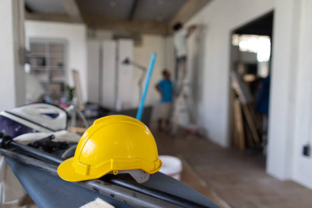 A repairman stands on a ladder and practices repairing a ceiling inside a house.