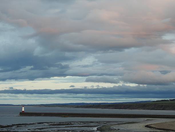 Evening view from the cliffs with dark sea at low tide and the lighthouse at the end of a long walkway