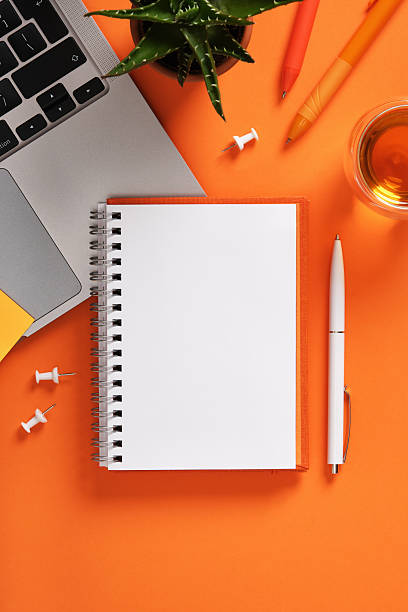 istock Blank notebook with laptop keyboard, pens, and cup of tea on orange desk. Workspace for study, planning, and creativity. 2232541337