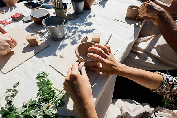 Hands carefully shape clay into small bowls at a pottery making workshop held outdoors. Participants are focused and enjoying the creative process surrounded by greenery.