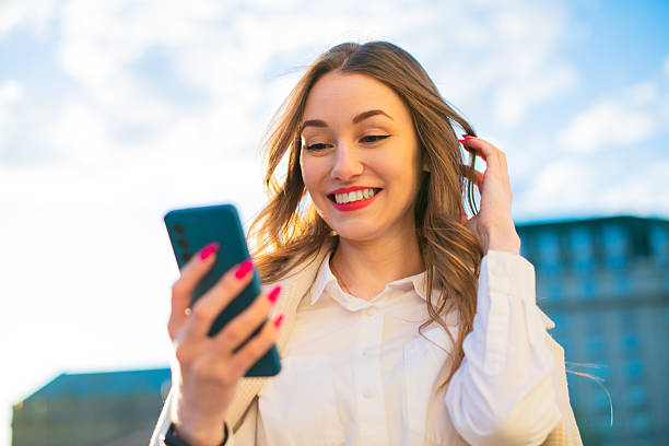 istock Smiling Fashionable Young Woman Using Smartphone Outdoors Under Blue Sky 2232550591