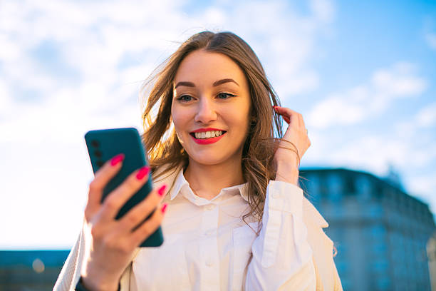 istock Smiling young female browsing smartphone outdoors in sunlight 2232550604