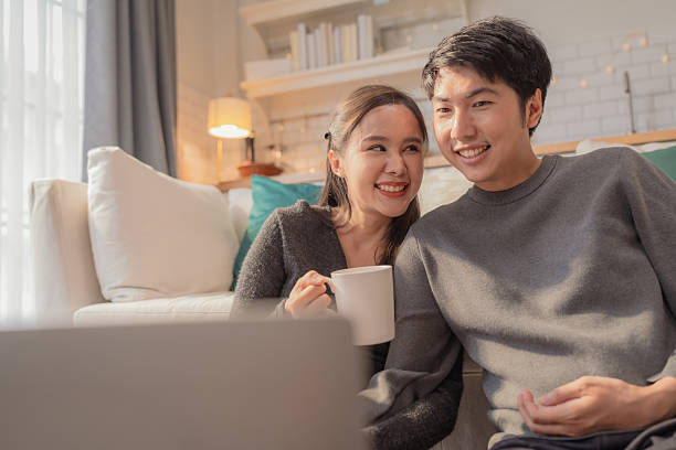 istock Asian marry couple is sitting on the floor at home, using a laptop computer watching media content online in a tablet in the living room while relax sit on floor daylight 2232555051
