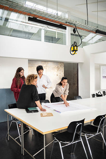 istock Architecture seminar with teacher and students collaborating on large blueprint design 2232558396