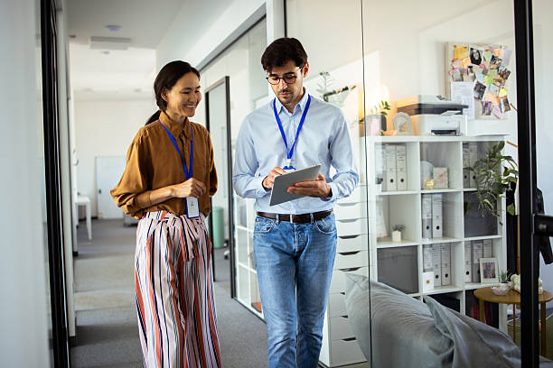 istock Two young business colleagues walking and talking in office corridor 2232561005
