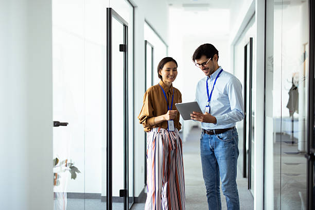 istock Smiling business colleagues using digital tablet in office corridor 2232561078