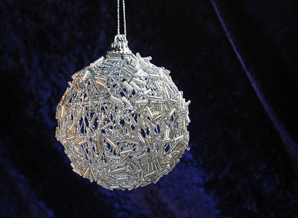 Sparkling silver christmas bauble hanging in front of dark blue velvet