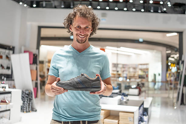 istock Man Smiling While Displaying a Stylish Shoe in a Mall 2232564756