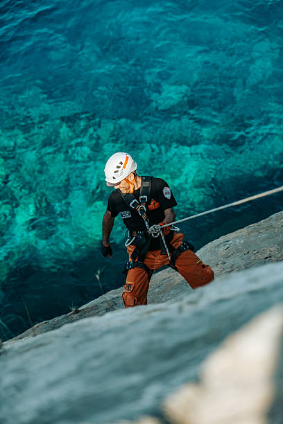 istock Climber with Helmet and Harness Rappelling Above Blue Sea 2232565096