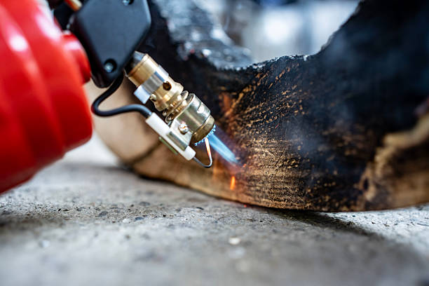 A detailed view of a blowtorch flame interacting with burnished wood on a concrete base, showcasing combustion processes.