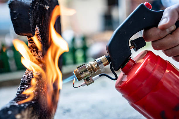 A blowtorch igniting a flame on a piece of wood. The image highlights the detail of the flame and wood texture, suggesting construction, tools, or creative burning techniques.