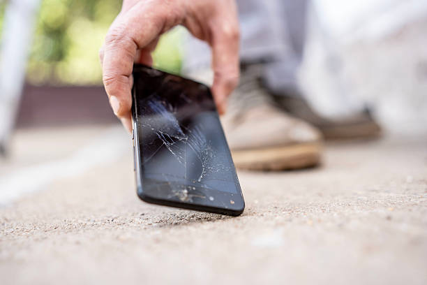 istock Person Picking Up a Broken Smartphone from the Ground Outside 2232565546