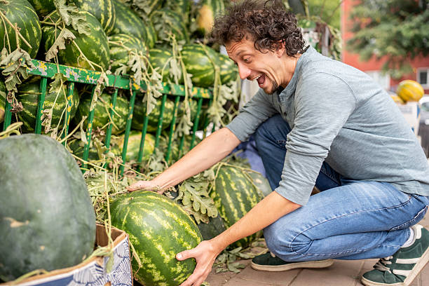 Man Enjoying Fresh Produce Selection Among Large Display of Watermelons